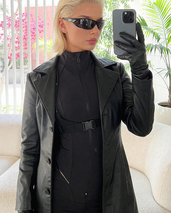 Mirror selfie of a blonde woman in a long black leather coat.
